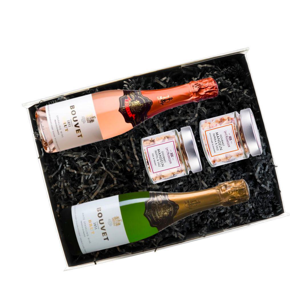 Geöffnete Geschenkbox mit Bouvet Brut & Rosé und zwei Gläsern Gourmet-Mandeln auf schwarzem Füllmaterial