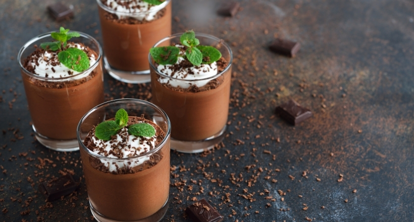 Vier Gläser mit leckerer Schokoladenmousse, verziert mit Sahne und Minzblättern auf einem dunklen Hintergrund