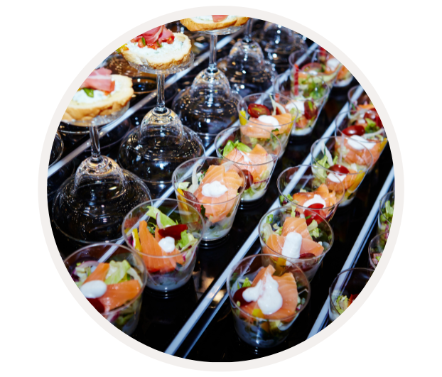 Nahaufnahme von stilvollen, in Gläsern servierten Salaten mit Lachs und cremigen Dressings, dekorativ angerichtet auf einem Buffet.
