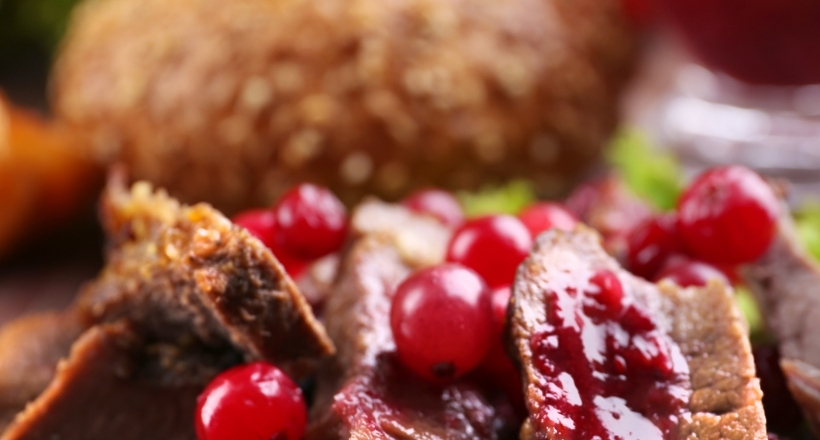 Nahaufnahme eines delikaten Wildfleischgerichts mit Preiselbeeren und einem Brotlaib im Hintergrund