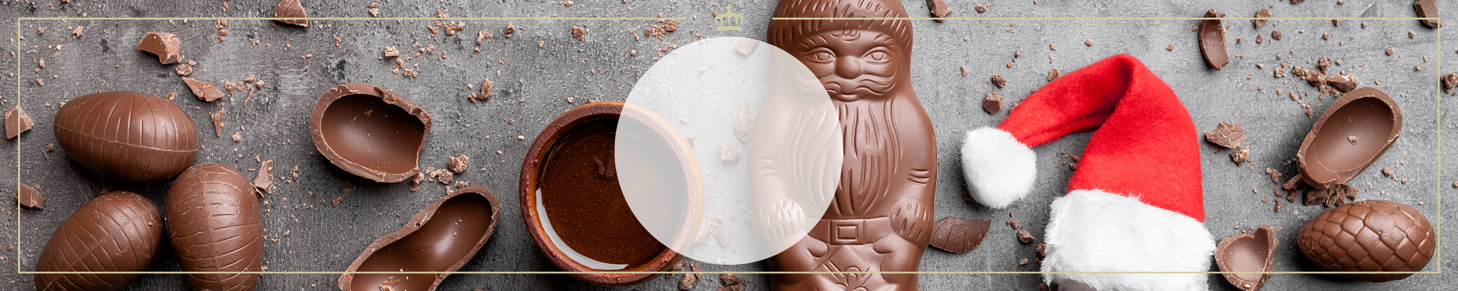 Verschiedene Schokoladeneier und ein Schokoladen-Nikolaus auf grauem Hintergrund, flankiert von roten Mützen und Schokoladenstücken