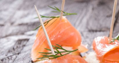 Appetithäppchen mit geräuchertem Lachs, garniert mit Dill und Zahnstocher serviert auf einem Holzbrett
