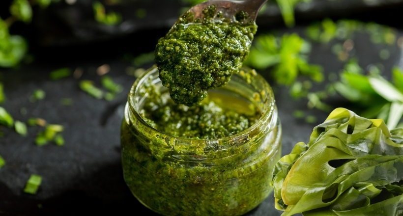Nahaufnahme eines Glases mit frischem grünem Pesto und einem Löffel