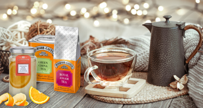 Stillleben mit Glastasse gefüllt mit Tee, umgeben von Assam- und grünem Tee in Verpackungen, Teekanne und Orangenscheiben auf einem rustikalen Holztisch.