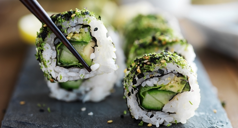 Nahaufnahme von Sushi-Rollen mit Avocado, Gurke und Sesam, serviert auf einer Schieferplatte