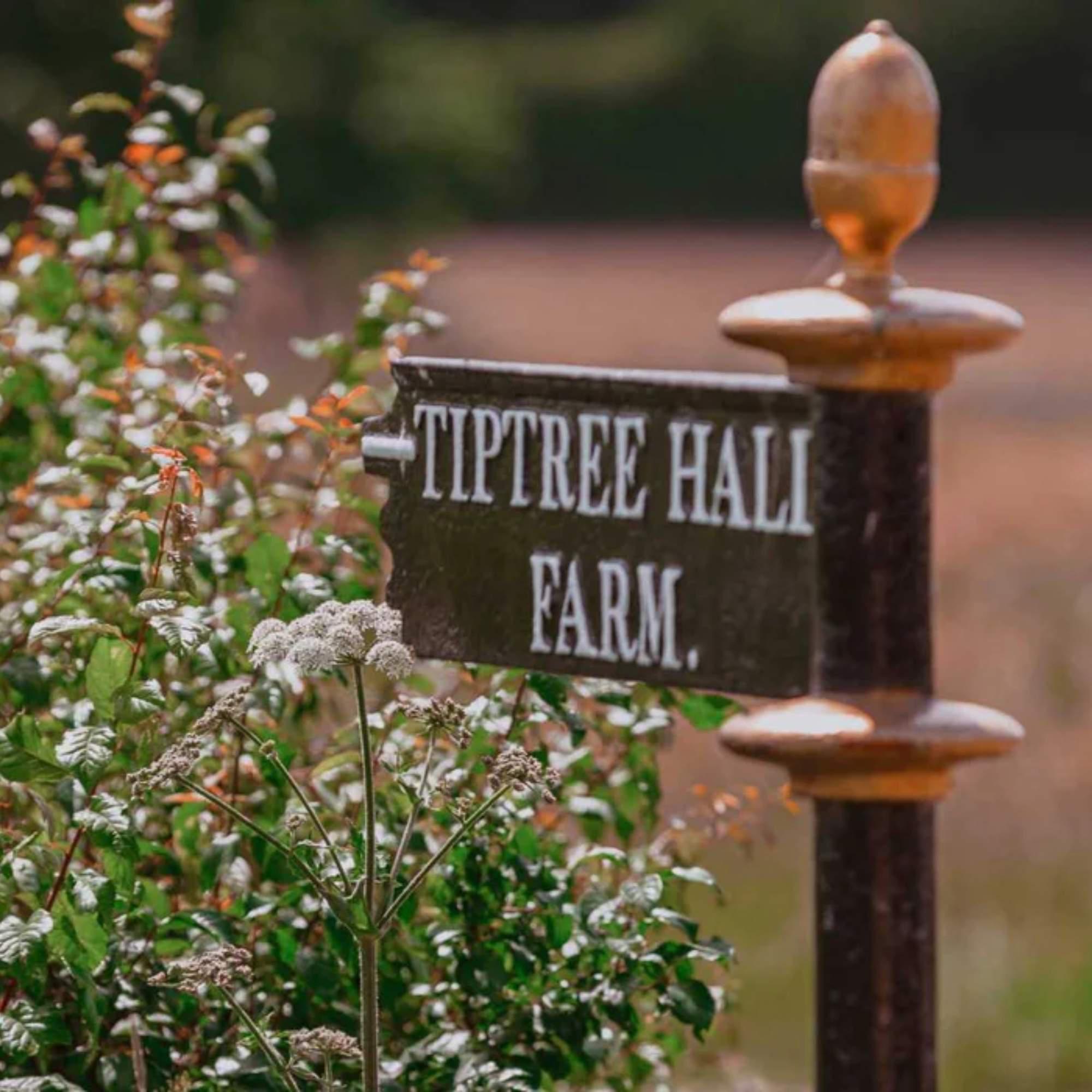 Schild „Tiptree Hall Farm" an einem Pfosten zwischen Wildblumen