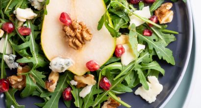 Nahaufnahme eines Rucola-Salats auf einem Teller, garniert mit Birnenscheiben, Walnüssen, Granatapfelkernen und Blauschimmelkäse