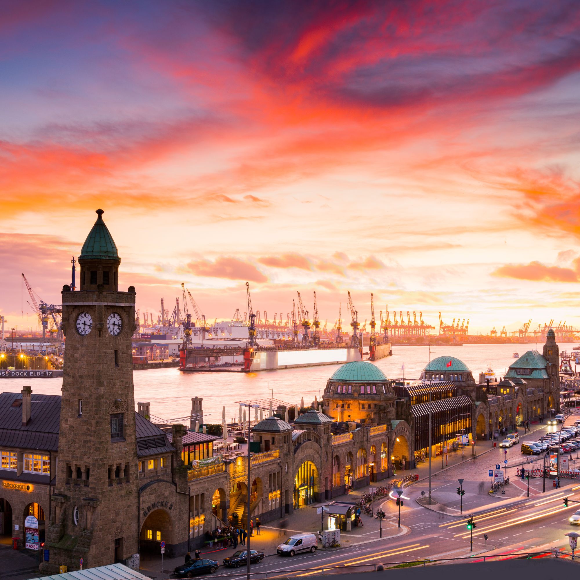 Blick auf den Hamburger Hafen bei Sonnenuntergang, mit den Landungsbrücken im Vordergrund und Kräne im Hintergrund