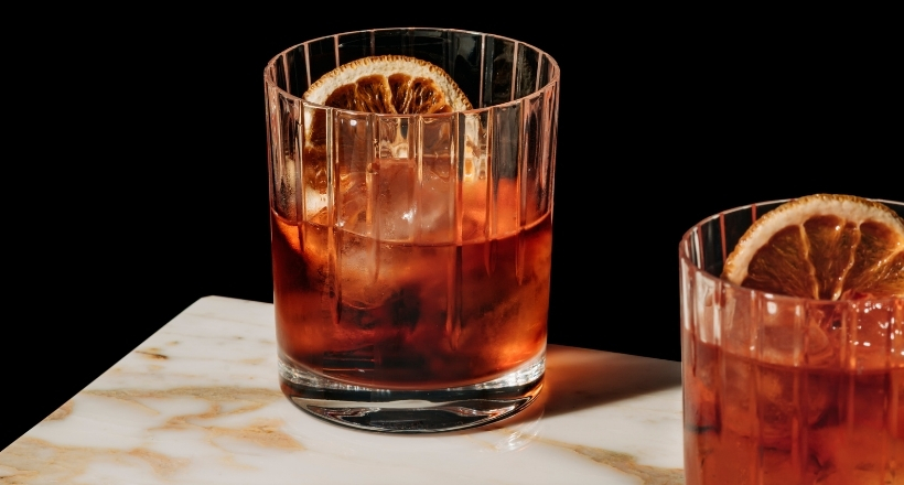 Zwei Cocktailgläser mit roten Getränken und Orangenscheiben auf einem Marmortisch