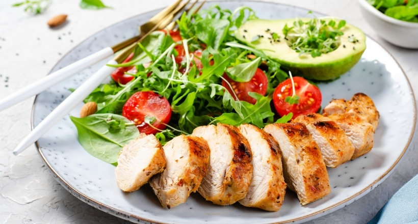 Ein Teller mit gegrilltem Hähnchen, Avocado, Rucola, Tomaten und frischem Gemüse.