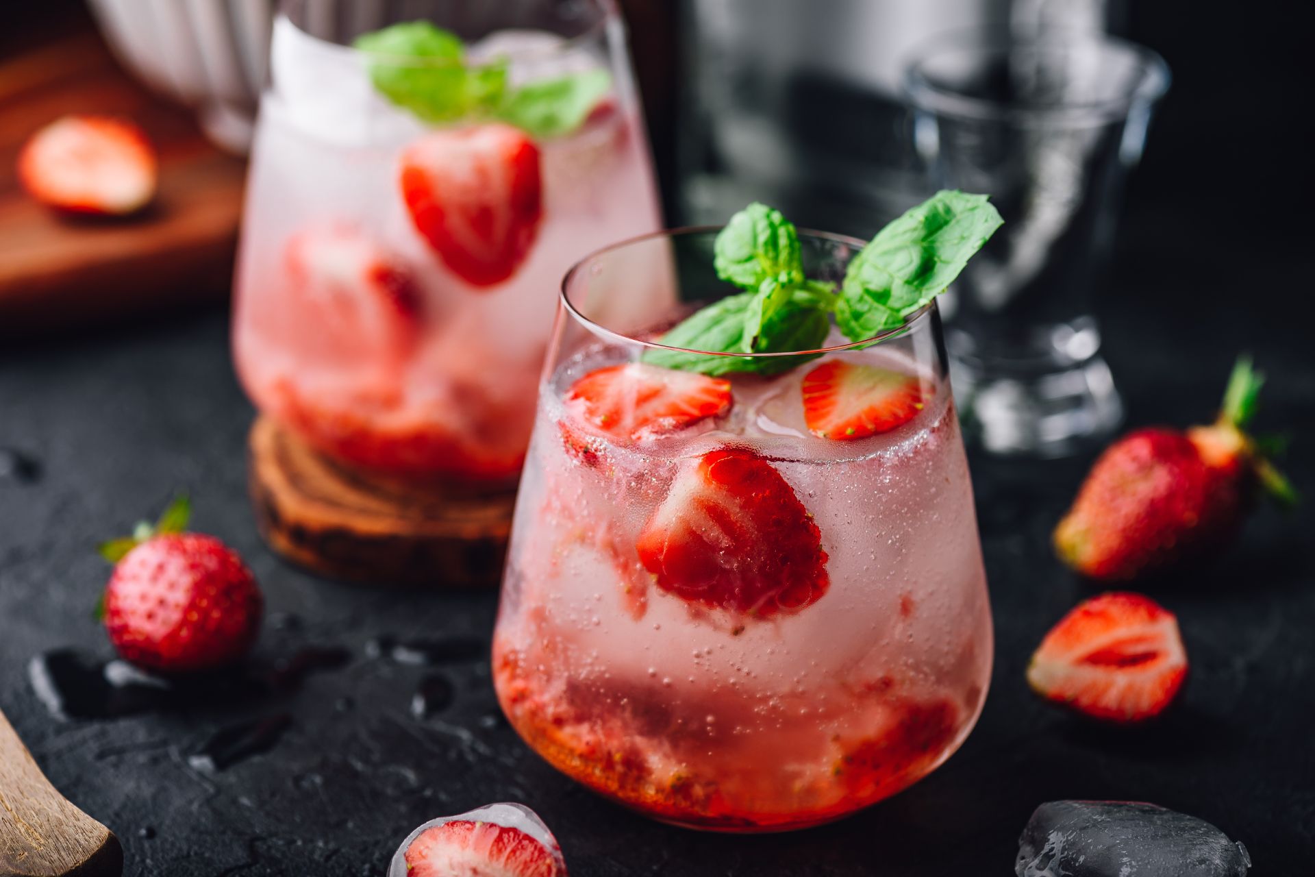 Zwei Gläser mit erfrischendem Erdbeer-Minz-Cocktail, verziert mit frischen Erdbeeren und Minzblättern, serviert mit Eiswürfeln auf einem dunklen Hintergrund