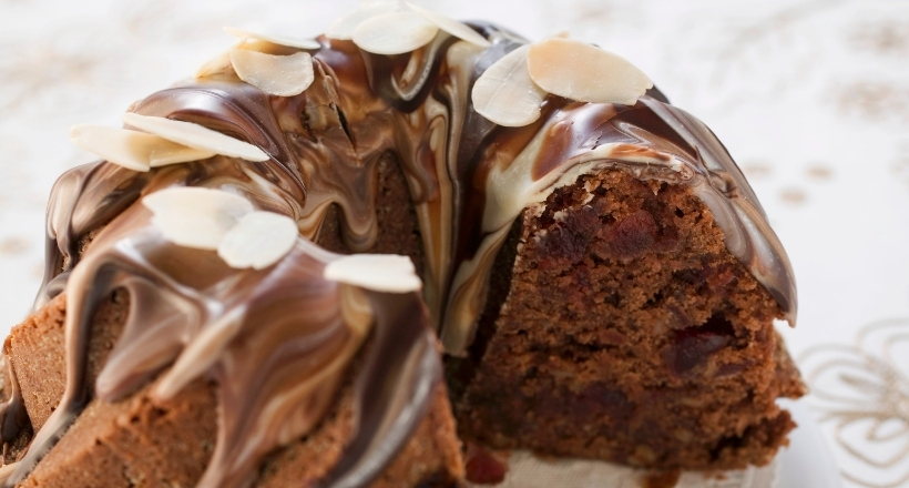 Ein köstlicher Schokoladen-Gugelhupf, verziert mit geschmolzener Schokolade und Mandelsplittern, angeschnitten auf einem Tisch mit floralem Muster