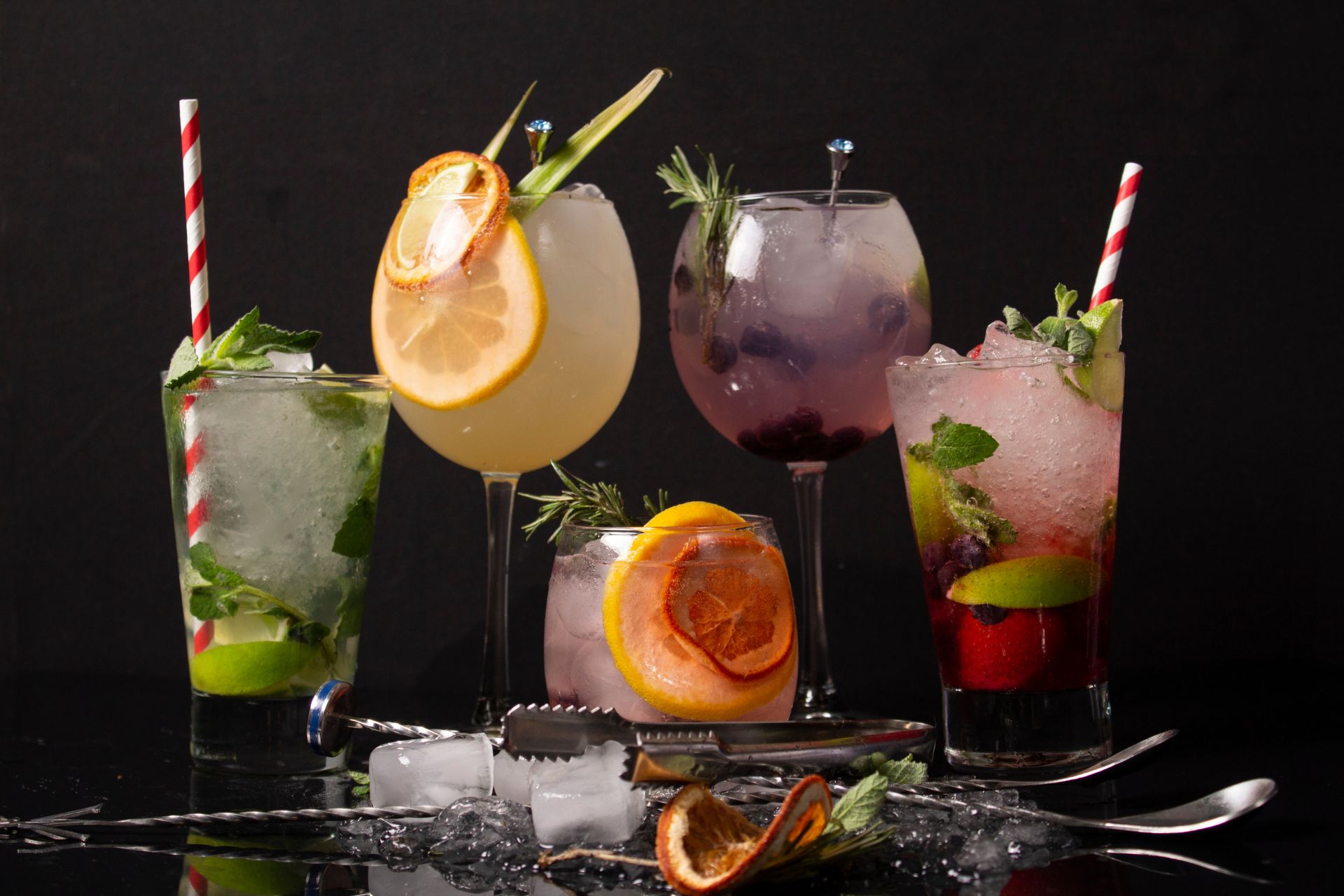 Verschiedene farbenfrohe Cocktails mit Obstscheiben, Minze und Eiswürfeln auf einem schwarzen Hintergrund