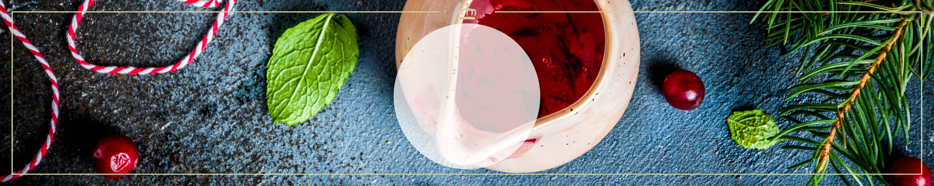 Nahaufnahme eines weihnachtlichen Getränks mit schwimmenden Cranberries, umgeben von Minzblättern und Tannenzweigen auf dunklem Hintergrund