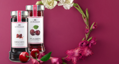 Zwei Gläser mit Kirsch- und Pflaumen-Marmelade, dekoriert mit Blumen auf rotem Hintergrund