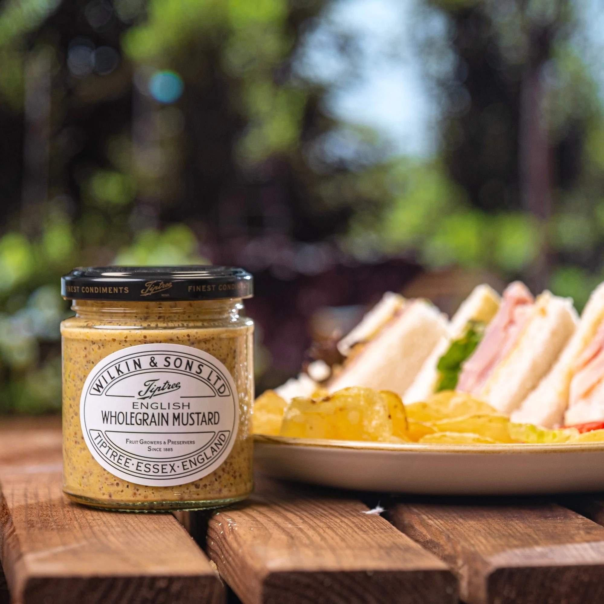 Tiptree Wilkin & Sons English Wholegrain Mustard im Glas neben Sandwiches auf Holztisch