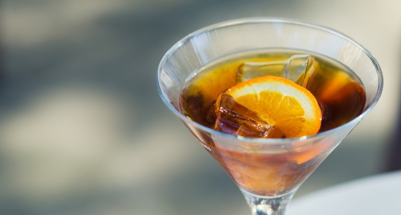 Nahaufnahme eines Cocktails im Glas mit Eiswürfeln und einer Orangenscheibe, serviert auf einem Tisch