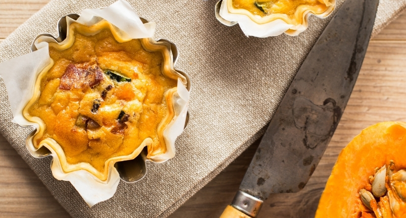 Frische Kürbis-Quiche mit Kürbis, in einer Backform gebacken, auf einem Holzbrett neben einem Messer