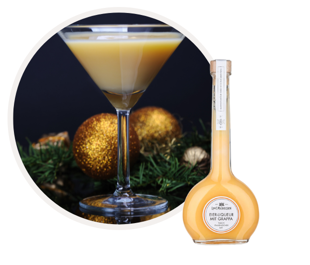 Flasche Eierlikör mit Grappa und gefülltes Cocktailglas, umgeben von weihnachtlicher Dekoration