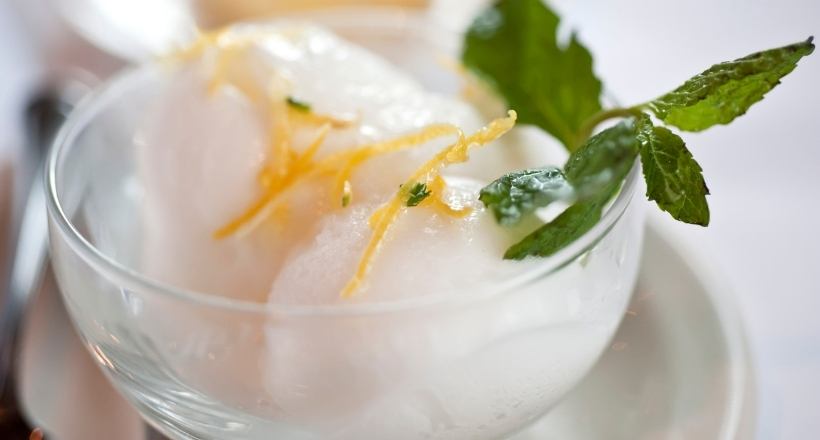 Zitronensorbet mit Zitronenzeste und Minzblatt in eleganter Glasschale serviert