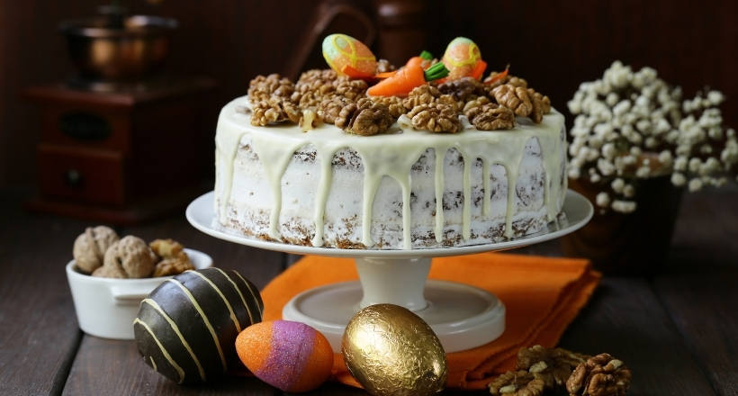 Ein ansprechend dekorierter Kuchen mit Walnüssen, Zuckereiern und glasiertem Guss, präsentiert auf einem weißen Kuchenteller, umgeben von Osterdekorationen.