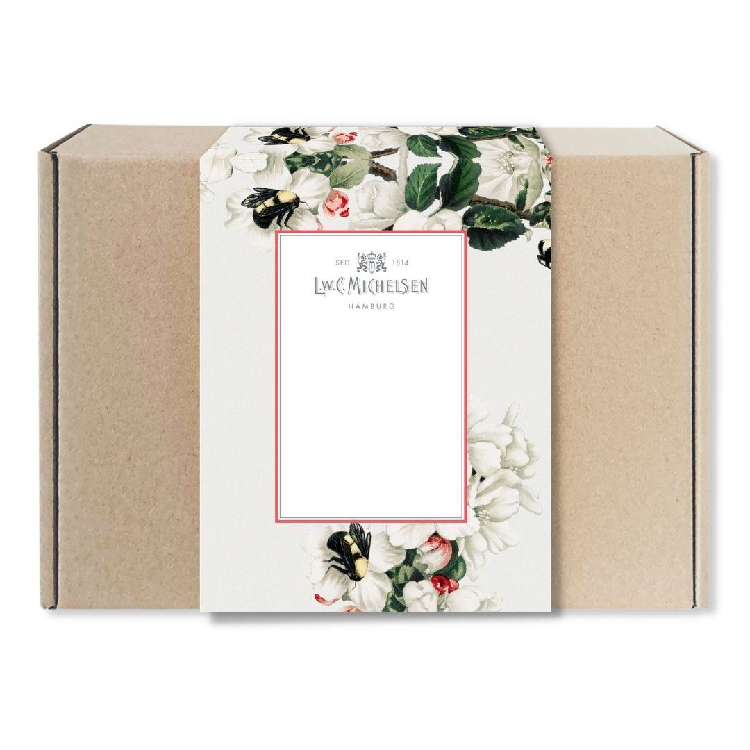 Geschlossene Geschenkbox aus braunem Karton mit dekorativer Banderole im floralen Design und Bienenmotiv sowie Logo von L.W.C. Michelsen Hamburg