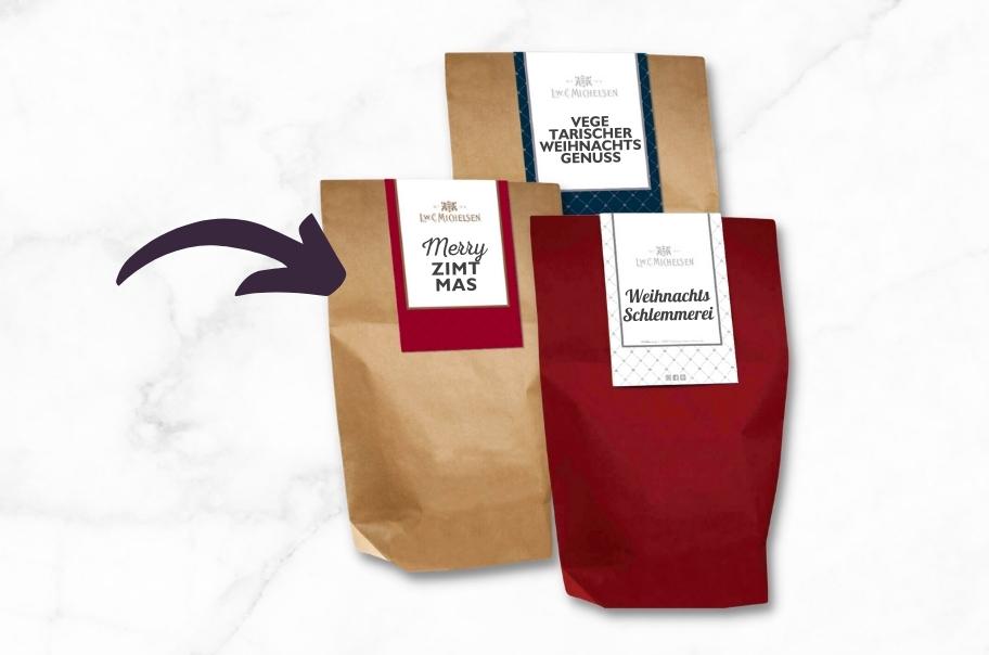 Drei weihnachtlich verpackte Genuss-Sets mit Aufschriften: Merry Zimtmas, Vegetarischer Weihnachtsgenuss und Weihnachtsschlemmerei